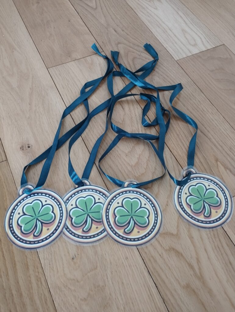  "Medallas de trébol plastificadas con cintas azules, hechas a partir de plantillas imprimibles, listas para ser usadas en celebraciones de St. Patrick’s Day.